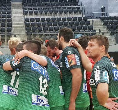 Handballspieler des SC Magdeburg umarmen sich jubelnd im Teamkreis auf dem Spielfeld.