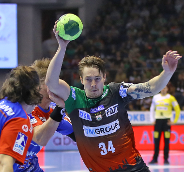 Handball-Actionaufnahme: SC-Magdeburg-Spieler Michael Damgaard (Nr. 34) springt hoch und wirft den Ball, während ein Verteidiger von HC Erlangen ihn zu stoppen versucht.