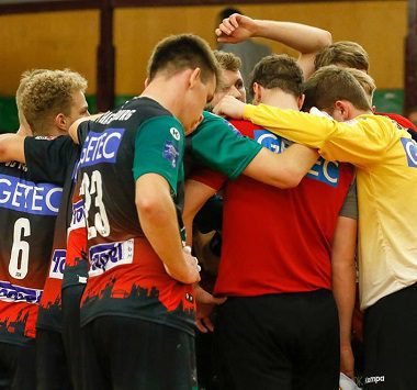 Teamkreis der SC Magdeburg nach der Heimniederlage gegen die Füchse Berlin: Spieler in grün-schwarzen und roten Trikots stehen eng zusammen und legen die Arme umeinander.