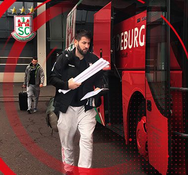 SCM-Trainer Bennet Wiegert steigt mit Unterlagen in der Hand aus dem roten Mannschaftsbus des SC Magdeburg.