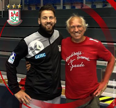 SCM-Trainer Bennet Wiegert lächelt für ein gemeinsames Foto neben einem Fahrradfahrer in einem roten „Handball Freunde Saale“-T-Shirt.