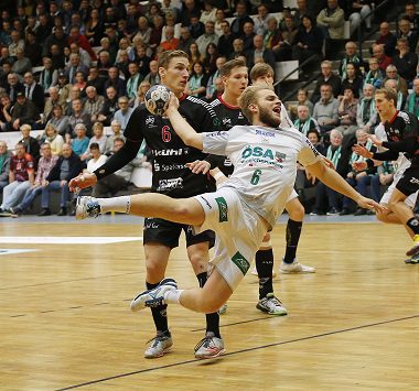 SCM-Nachwuchsspieler Alex Reimann (Nummer 6) im weißen Trikot beim Sprungwurf aus dem Rückraum, verfolgt von einem Gegenspieler in Schwarz.