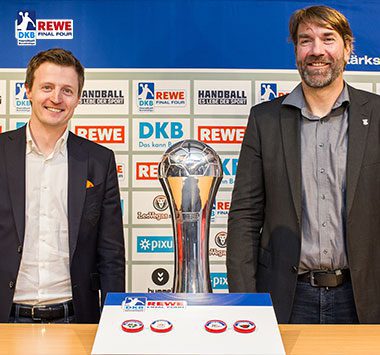 SCM-Geschäftsführer Marc-Henrik Schmedt (rechts) posiert zusammen mit einem Verantwortlichen der Handball-Bundesliga und dem DHB-Pokal bei der Halbfinal-Auslosung des REWE Final Four.