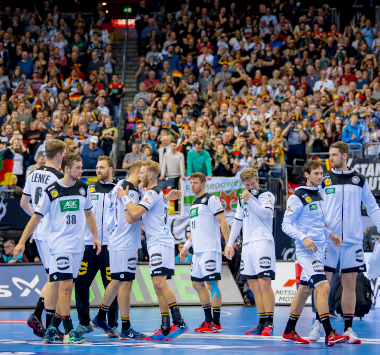 Die Spieler der deutschen Nationalmannschaft klatschen sich im weißen DHB-Trikot vor der gut besuchten Zuschauertribüne in Köln ab