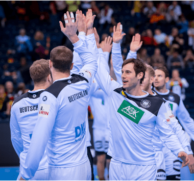 Mehrere Spieler der deutschen Handballnationalmannschaft geben sich auf dem Spielfeld ein High Five.