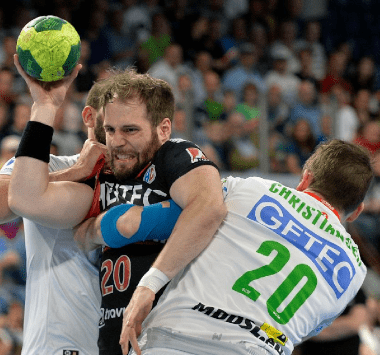 SCM-Handballspieler Matthias Musche behauptet im weißen Trikot den Ball im dichten Zweikampf gegen zwei Gegenspieler.