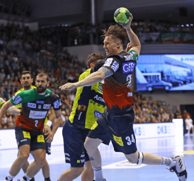 Ein Handballspieler des SC Magdeburg setzt im dunkelblauen Trikot im Sprungwurf zum Torabschluss an.