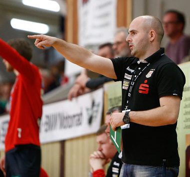 Handballtrainer steht am Spielfeldrand und gibt mit ausgestrecktem Arm Anweisungen.