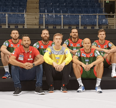 Die Neuzugänge des SC Magdeburg, darunter Christoph Steinert und Erik Schmidt, sitzen gemeinsam mit dem Trainerteam für ein Foto auf der Bank.
