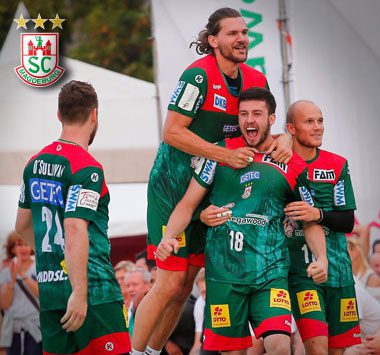 Die SC Magdeburg Handballer Michael Damgaard (Nummer 18), Christian O'Sullivan (Nummer 24) und Filip Kuzmanovski jubeln gemeinsam ausgelassen auf dem Spielfeld.
