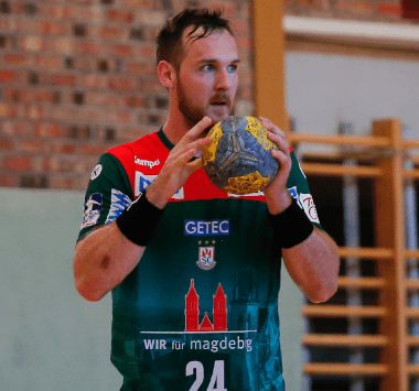 SC Magdeburg Handballer Christian O'Sullivan (Nummer 24) blickt konzentriert mit dem Ball in beiden Händen.