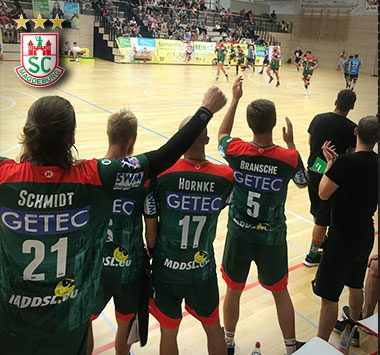 Spieler des SC Magdeburg (unter anderem mit den Trikotnummern 21, 17 und 5) verfolgen von der Bank aus das Spielgeschehen in der Halle in Halle (Saale) und unterstützen ihr Team.