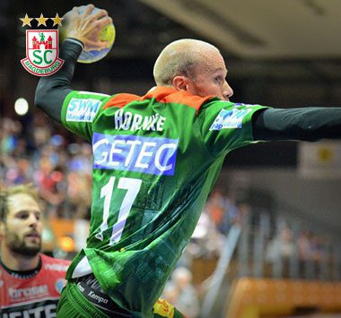 Handballspieler Tim Hornke mit der Trikotnummer 17 im grün-roten Dress des SC Magdeburg fängt den Ball in der Luft.