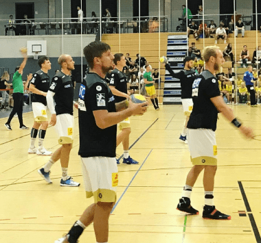 Handballspiel in einer Sporthalle: Mehrere Spieler des SC Magdeburg in schwarzen Trikots und weißen Hosen laufen sich vor dem Spiel warm.