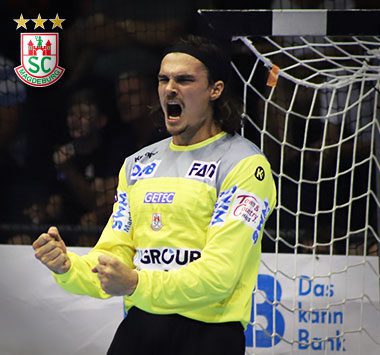 Handball-Torwart Jannick Green im gelben Trikot des SC Magdeburg jubelt emotional mit geballten Fäusten und geöffnetem Mund vor dem Tornetz.