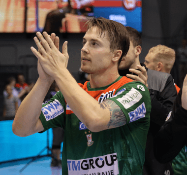 Rückraumspieler Michael Damgaard im grün-roten Trikot des SC Magdeburg applaudiert mit erhobenen Händen den Fans in der Halle.