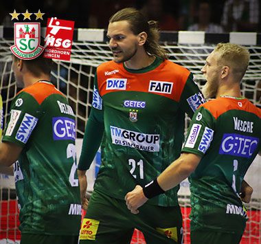 Drei Handballspieler des SC Magdeburg in grün-roten Trikots, darunter Christian O'Sullivan mit der Nummer 21 und Matthias Musche (rechts), besprechen sich fokussiert auf dem Spielfeld.