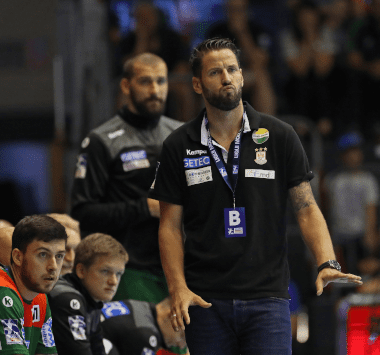 SCM-Trainer Bennet Wiegert steht im schwarzen Poloshirt mit einer Akkreditierungskarte um den Hals am Spielfeldrand und gibt mit ausgestrecktem Arm taktische Anweisungen.