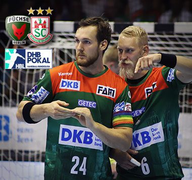 Die Handballspieler Christian O'Sullivan (Trikotnummer 24) und Matthias Musche (Trikotnummer 6) stehen im grün-roten SCM-Trikot nebeneinander auf dem Spielfeld und blicken fokussiert nach vorne.