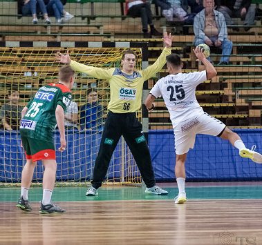 Ein Handballspieler der HG Hamburg-Barmbek (Nummer 25) wirft im weißen Trikot aufs Tor, während Magdeburgs Torwart mit gehobenen Armen pariert.