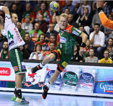 Handballspieler Matthias Musche springt im grün-roten Magdeburg-Trikot für einen Wurf hoch in die Luft, während ein Göppinger Abwehrspieler versucht, ihn zu stoppen.