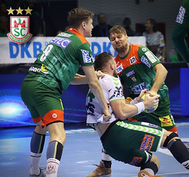 Die Handballspieler Christoph Steinert und Marko Bezjak (SC Magdeburg) packen im grün-roten Trikot gemeinsam in der Abwehr gegen einen Hannoveraner Angreifer zu