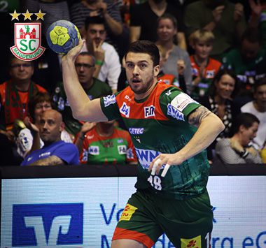 Handballspieler Filip Kuzmanovski holt im grün-roten Trikot des SC Magdeburg mit dem Ball in der rechten Hand zum Wurf aus.