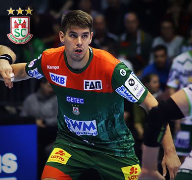 Handballspieler Piotr Chrapkowski blickt im grün-roten Trikot des SC Magdeburg aufmerksam und konzentriert auf das Spielgeschehen.
