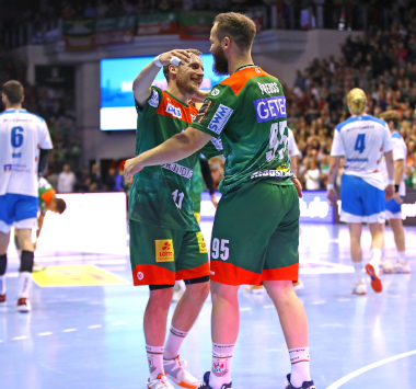 Die Magdeburger Handballspieler Michael Damgaard und Moritz Preuss jubeln gemeinsam im grün-roten Trikot auf dem Spielfeld.