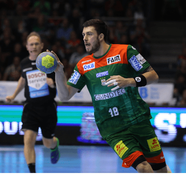 Handballspieler Filip Kuzmanovski läuft im grün-roten Trikot des SC Magdeburg mit dem Ball in der Hand an einem gegnerischen Spieler vorbei.