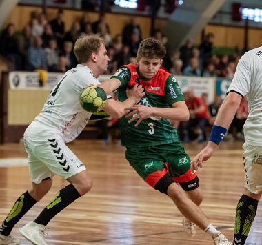 Ein Handballspieler des SC Magdeburg II (Nummer 3) wird im grün-roten Trikot beim Angriffsversuch von einem Schweriner Abwehrspieler in Weiß bedrängt.