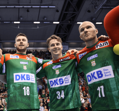 Die Magdeburger Handballspieler Filip Kuzmanovski, Michael Damgaard und Daniel Pettersson jubeln Arm in Arm im grün-roten Trikot.