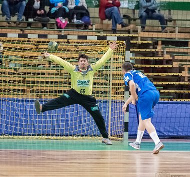 Ein Handballspieler des HC Empor Rostock wirft im blauen Trikot aufs Tor, während der Torwart des SC Magdeburg II (Nummer 83) vergeblich im Sprung pariert.