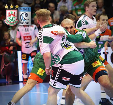 Handballspieler Željko Musa packt im grün-roten Trikot des SC Magdeburg in der Abwehr fest gegen einen weiß-grünen Angreifer von Górnik Zabrze zu.