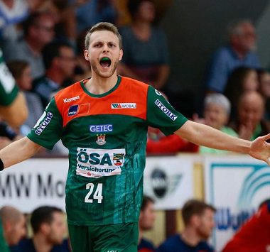 Ein Handballspieler des SC Magdeburg II (Nummer 24) jubelt mit weit aufgerissenem Mund und ausgebreiteten Armen im grün-roten Trikot.