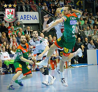 Handballspieler Christian O'Sullivan springt im grün-roten Magdeburg-Trikot (Nummer 24) frei zum Wurf ab, während sein Teamkollege Moritz Preuss am Boden zusieht.