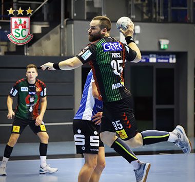 Spielszene beim Handball: SCM-Kreisläufer Moritz Preuss (Nummer 95) setzt sich am Kreis im Sprungwurf gegen die gegnerische Abwehr in Blau-Weiß durch.