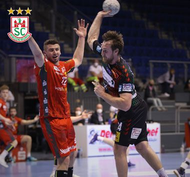 Handball-Spielszene: SCM-Kapitän Christian O'Sullivan bricht im schwarz-rot gestreiften Heimtrikot mit dem Ball in der Hand durch, während ein Essener Abwehrspieler (Nummer 22) in Rot hinterherläuft.