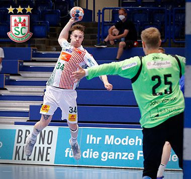 Michael Damgaard (Nummer 34) zieht im weißen SCM-Trikot im Sprungwurf ab, während Lemgo-Torwart Peter Johannesson (Nummer 25) abwehrt.
