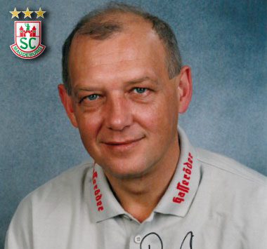 Archiv-Porträtfoto des ehemaligen SCM-Spielers und Trainers Peter Rost in einem hellen Hemd mit rotem Kragenaufdruck.