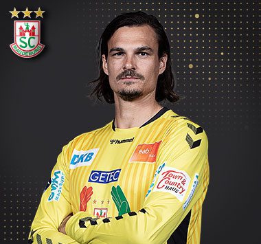 Porträtfoto von Torwart Jannick Green im gelben Torwarttrikot des SC Magdeburg mit SCM-Logo oben links.