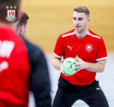 Lukas Mertens im roten Nationalmannschafts-Trikot hält fokussiert einen Handball mit beiden Händen.
