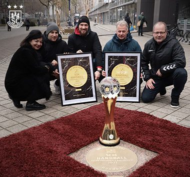 Vier Personen präsentieren eine neue Bodenplatte und die IHF Super Globe Trophäe auf dem Sports Walk of Fame.