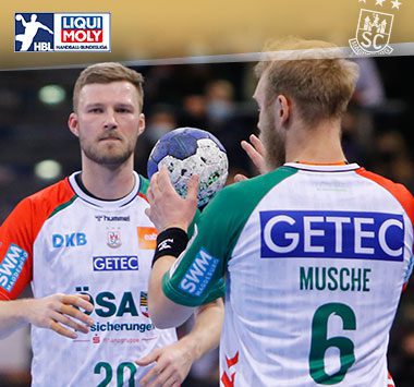 Philipp Weber schaut im weißen Trikot des SC Magdeburg mit dem Handball in der Hand zu Matthias Musche.