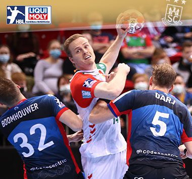 Ómar Ingi Magnússon zieht im weißen Trikot des SC Magdeburg zum Torwurf gegen zwei Abwehrspieler von Bergisch HC ab.