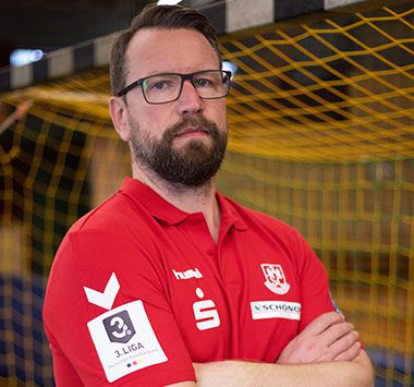 Stephan Just blickt im roten Vereinstrikot des SC Magdeburg mit verschränkten Armen nach vorne.
