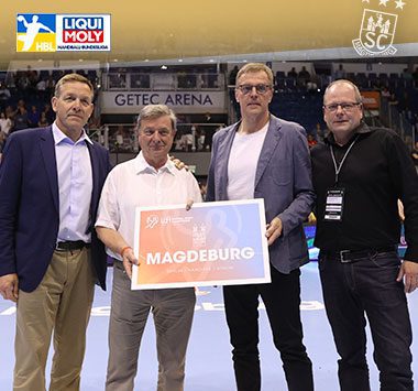 Vier Funktionäre posieren in der GETEC Arena und halten eine offizielle Magdeburg-Spielortkarte zur U21-WM.