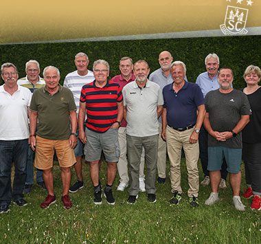 Ehemalige Handballer des SC Magdeburg posieren gemeinsam für ein Gruppenfoto auf einer Wiese.