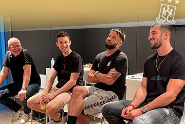 Vier Männer sitzen gut gelaunt auf Hockern bei einem Fantreffen in der Arena.