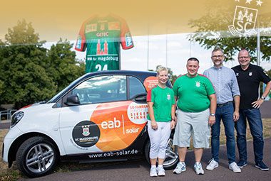 Die Gewinner des Tippspiels posieren lächelnd in grün-weißen SCM-Shirts neben einem eab-solar Werbeauto.